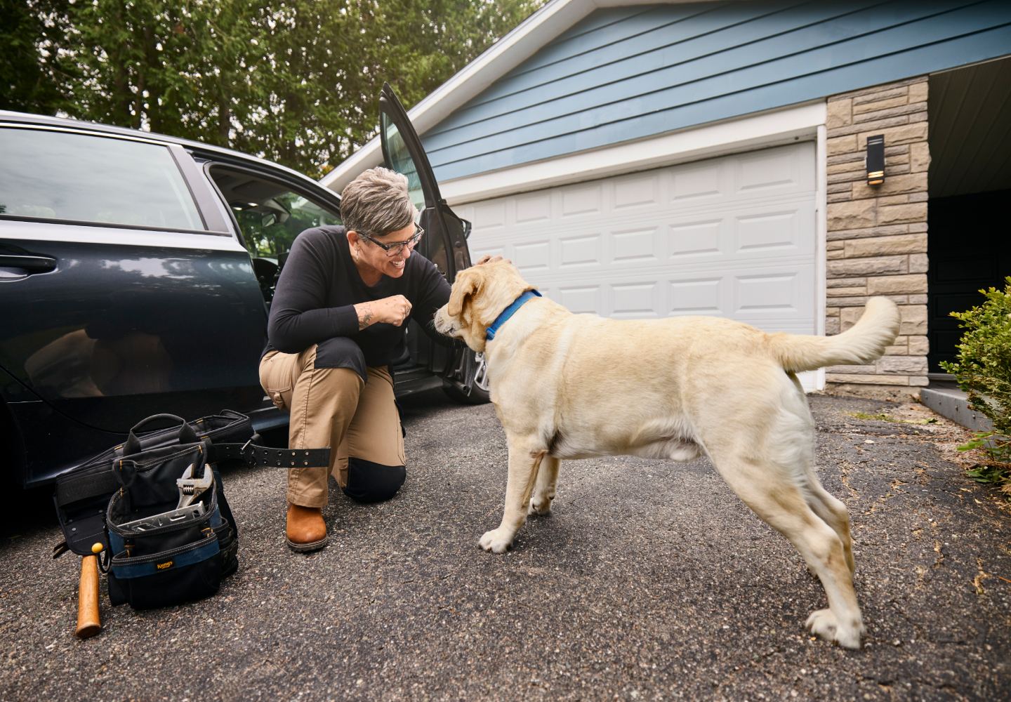 A homeowner crouching to greet their dog in the driveway